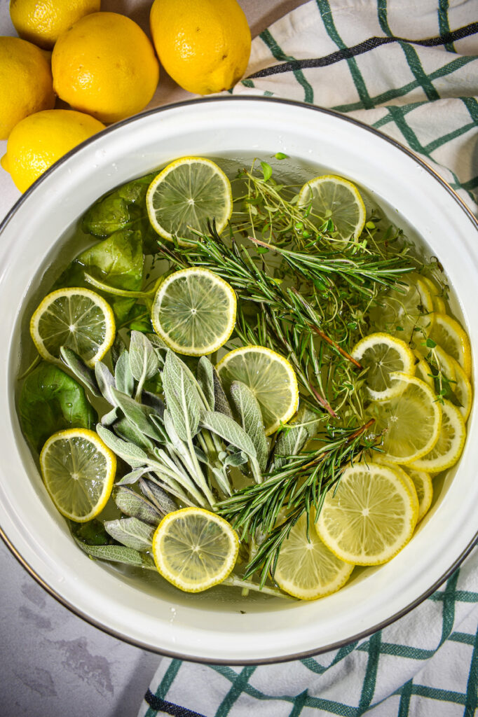 Herb and citrus simmer pot on a white surface with a plaid towel and yellow lemons