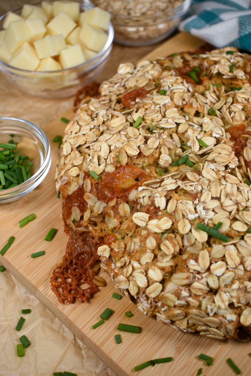 soda bread with cheddar and herbs on a wooden cutting board with dishes of chives, oats, and cubed cheese