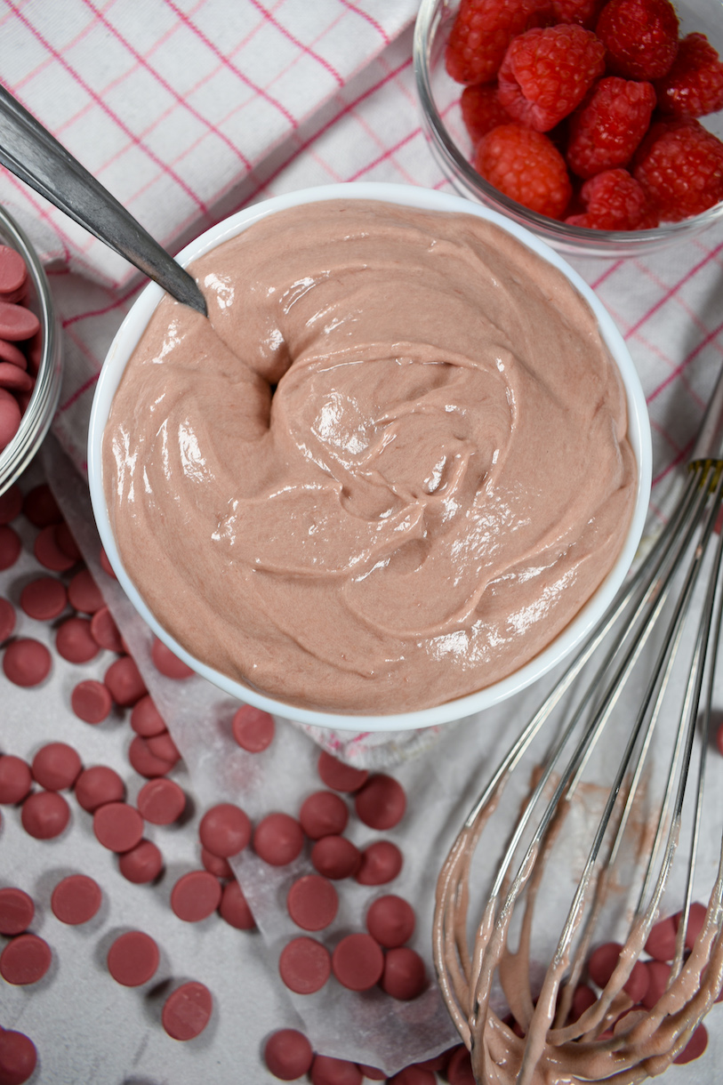 A bowl of ruby chocolate ganache with raspberries, ruby callets, and a whisk