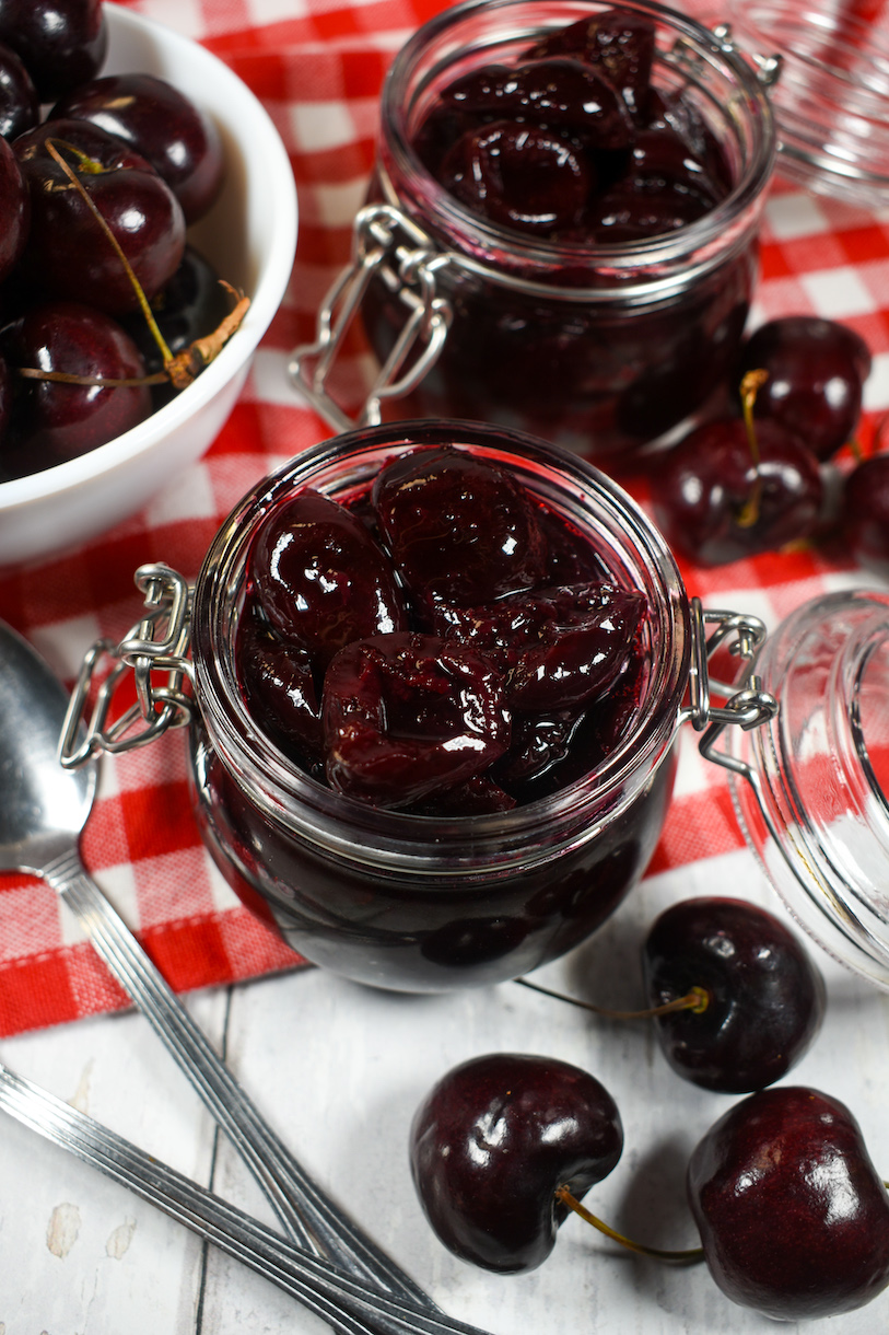 jars of homemade cherry compote, fresh cherries, and a red gingham tea towel
