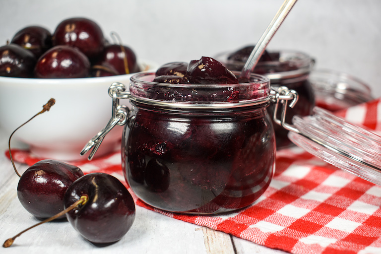 a jar of cherry compote and dish of fresh cherries on a red gingham towel