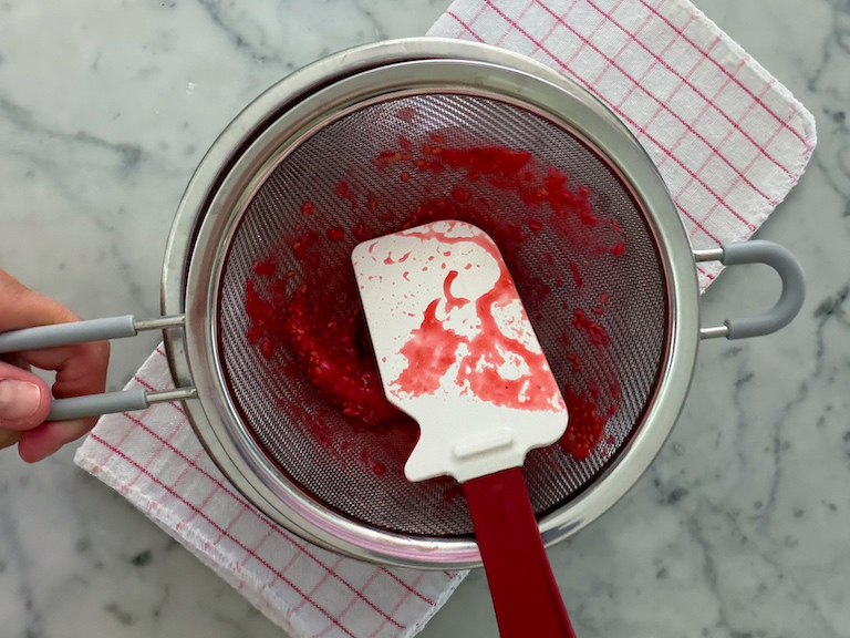 passing puréed raspberries through a mesh strainer