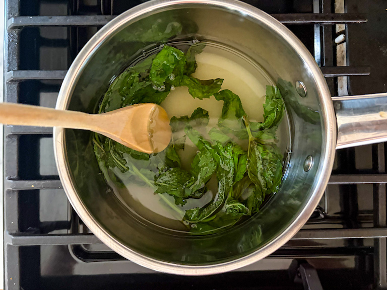 Stirring together mint leaves, sugar, and water in a small pan on the stovetop