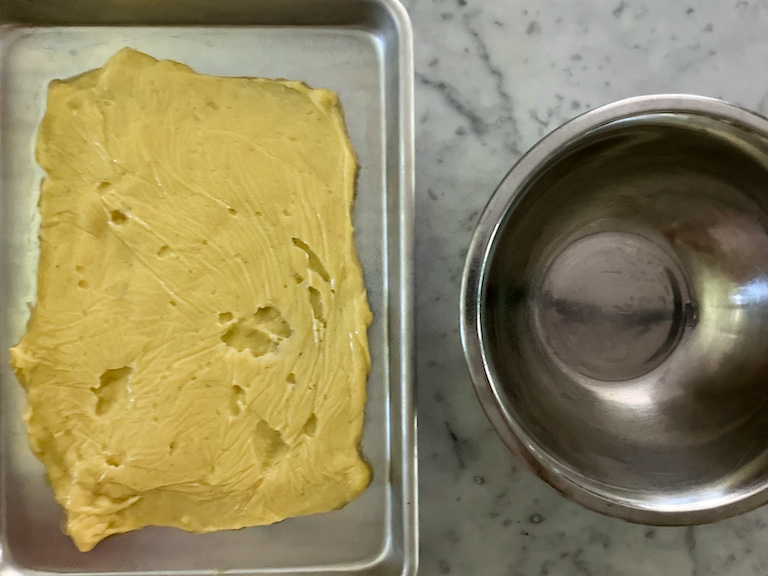 a tray of pastry cream and a metal mixing bowl on a marble surface