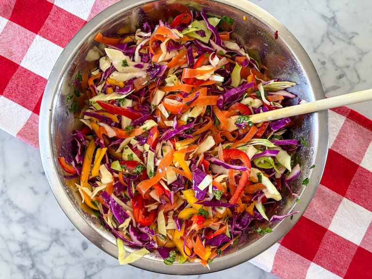 bowl of rainbow coleslaw arranged on a red checkered tea towel