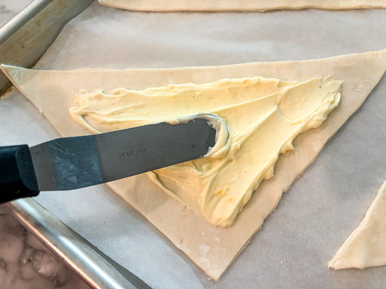 A small palette knife spreading mascarpone cheese over puff pastry