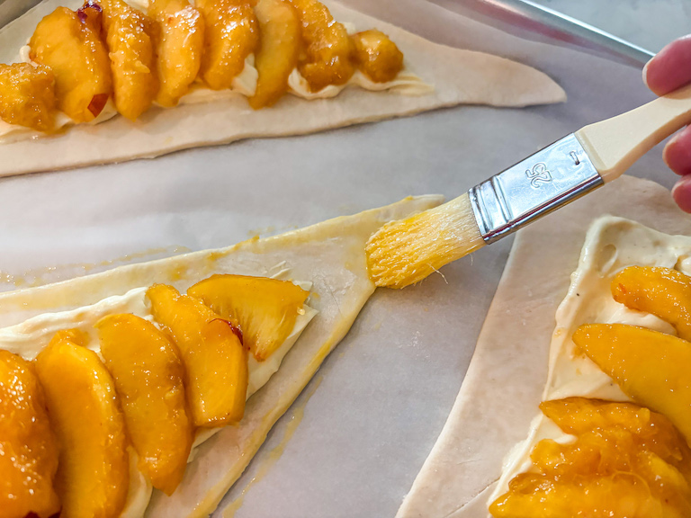 pastry brush egg-washing the edges of a puff pastry triangle