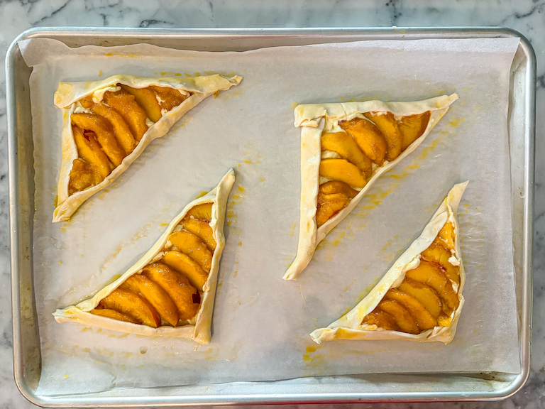 four peach mascarpone pastries arranged on a tray before baking