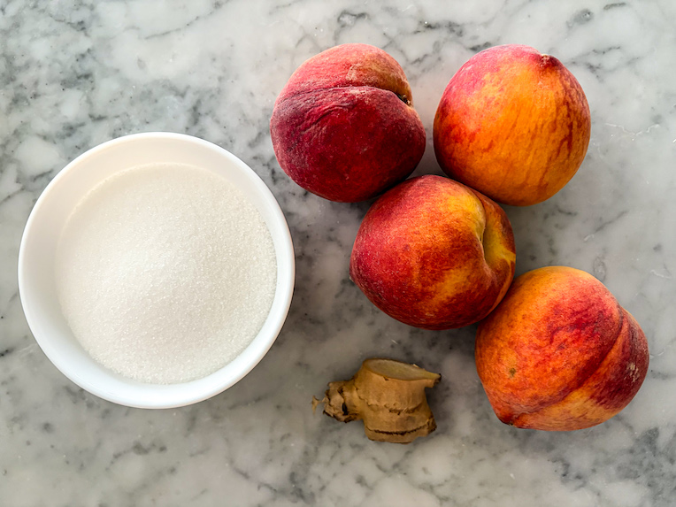 peaches, fresh ginger root, and dish of sugar on a marble surface