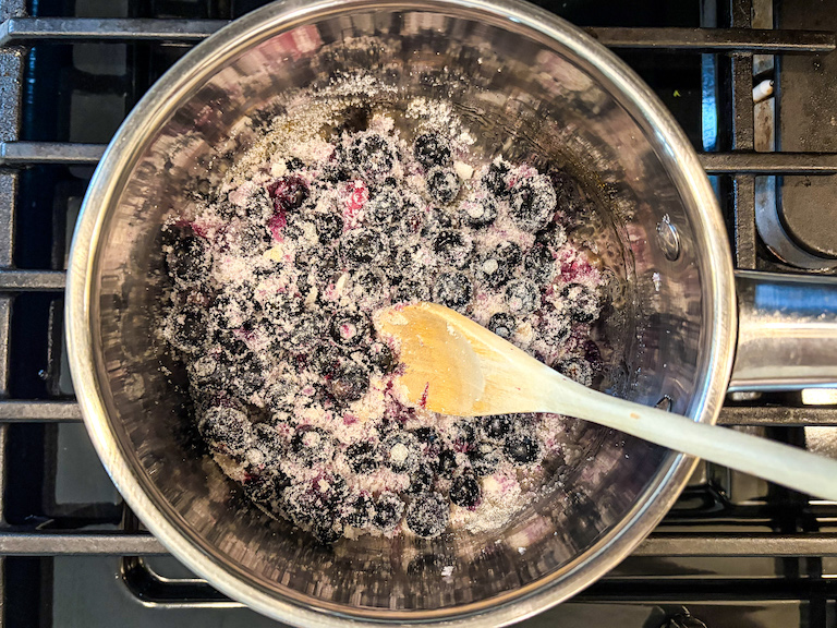 sugar and berries in a pan with a wooden spoon