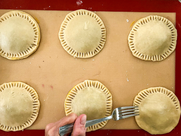 fork crimping edges of a tray of round hand pies