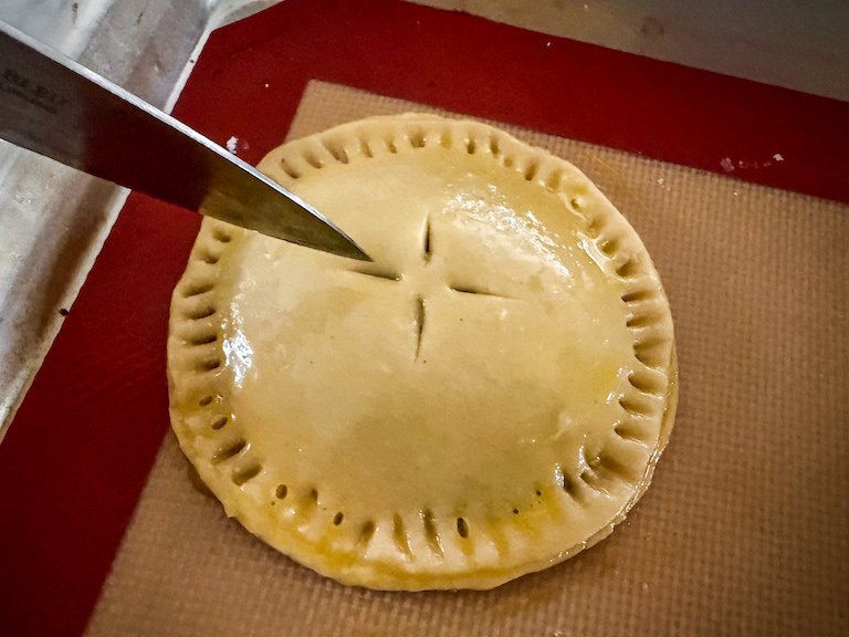 knife slicing vents in the top of an unbaked hand pie