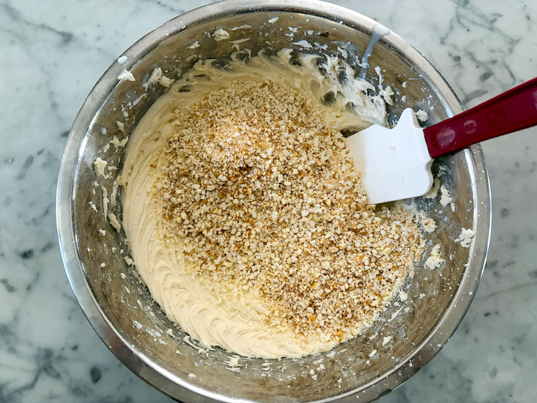 adding crushed caramel corn to a bowl of buttercream frosting