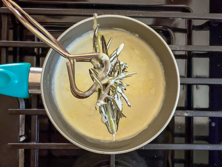 removing rosemary from a pan of cream with kitchen tongs