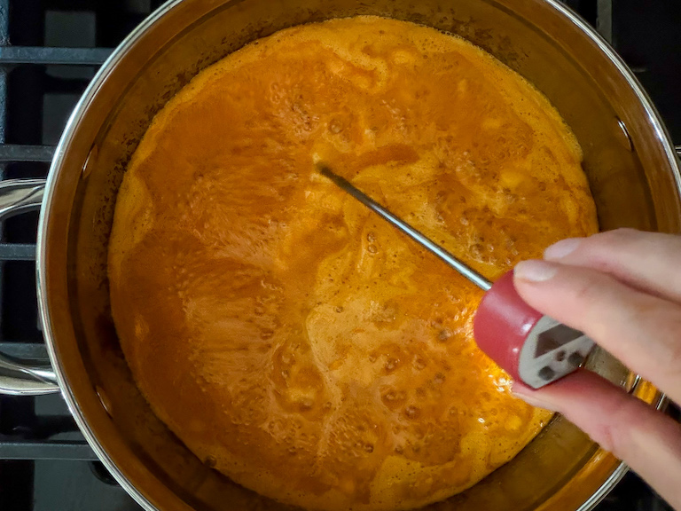 hand taking temperature of carrot candy syrup