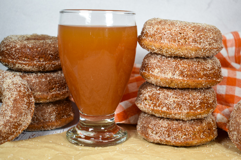 a stack of apple cider donuts and glass of cider