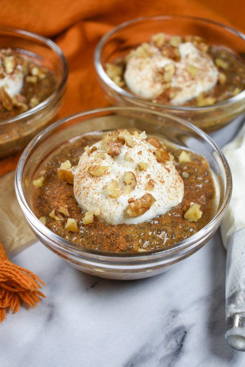 dish of pumpkin spice chia seed pudding garnished with nuts, cinnamon, and whipped cream
