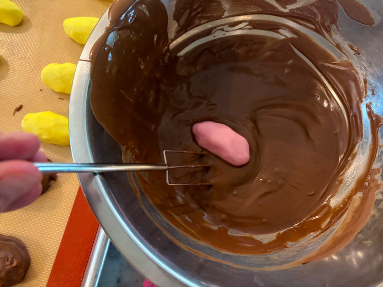 enrobing a pink egg in melted chocolate
