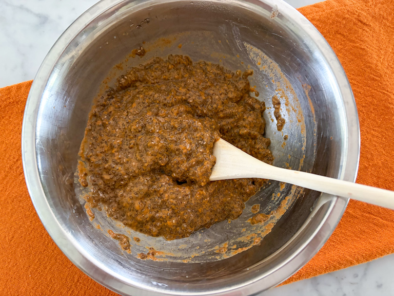 a mixing bowl of pumpkin spice chia seed pudding with a wooden spoon