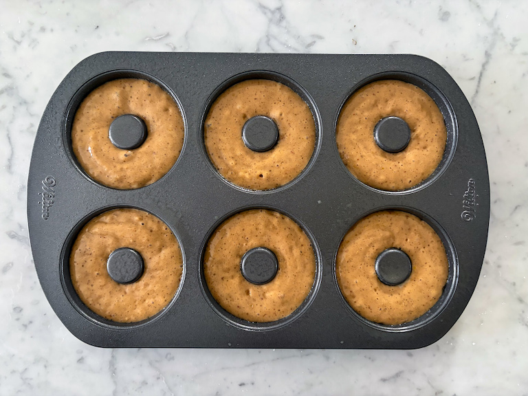 donut batter piped into a metal donut pan