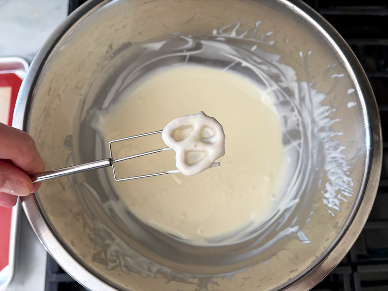 dipping a pretzel in melted white chocolate