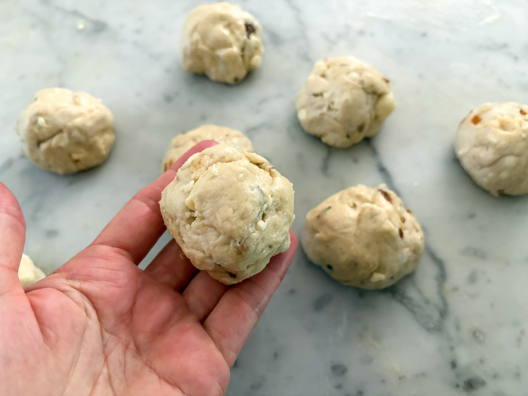 hand holding a ball of dough shaped into a bread roll
